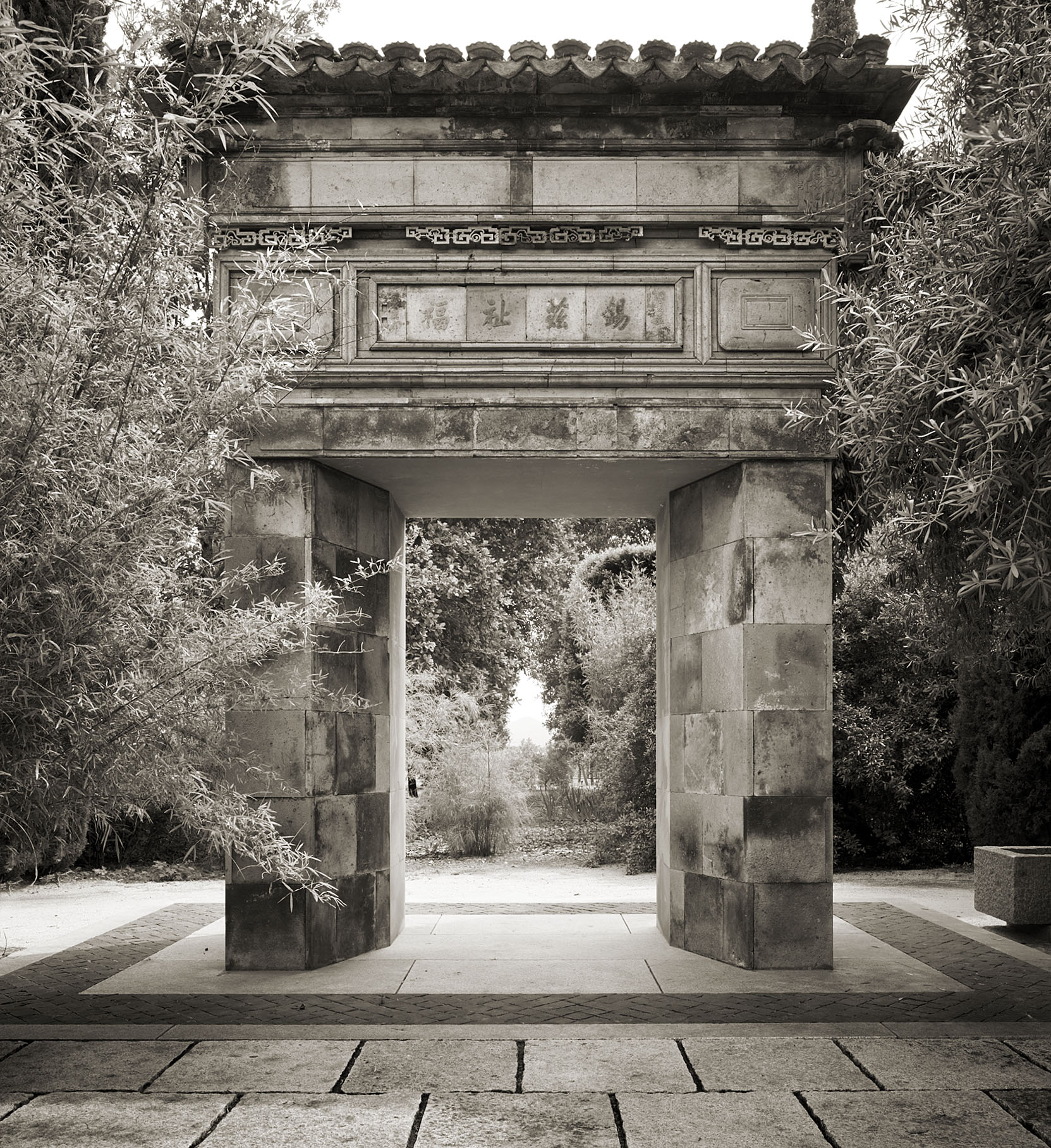 Historic stone archway at the entrance of Round Pond Estate, surrounded by lush trees and traditional Chinese architecture.