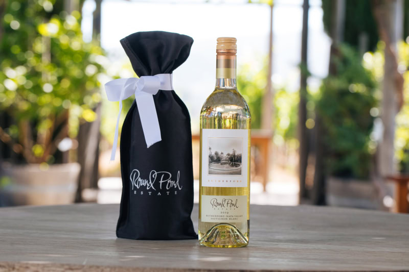 Elegant wine bottle from Round Pond Estate with a black gift bag, set outdoors on a wooden table.