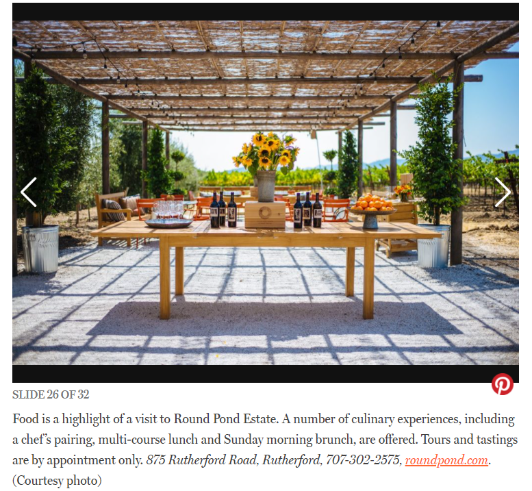 Outdoor dining setup at Round Pond Estate with a wooden table, sunflowers, and a scenic vineyard backdrop.