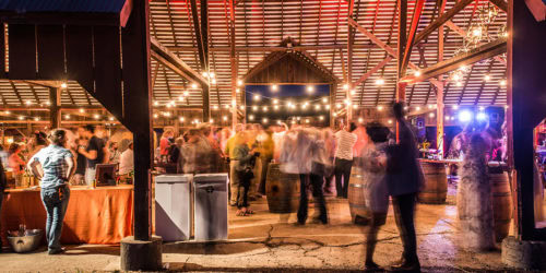 Guests enjoying a lively evening event at Round Pond Estate with string lights and music in a rustic barn setting.