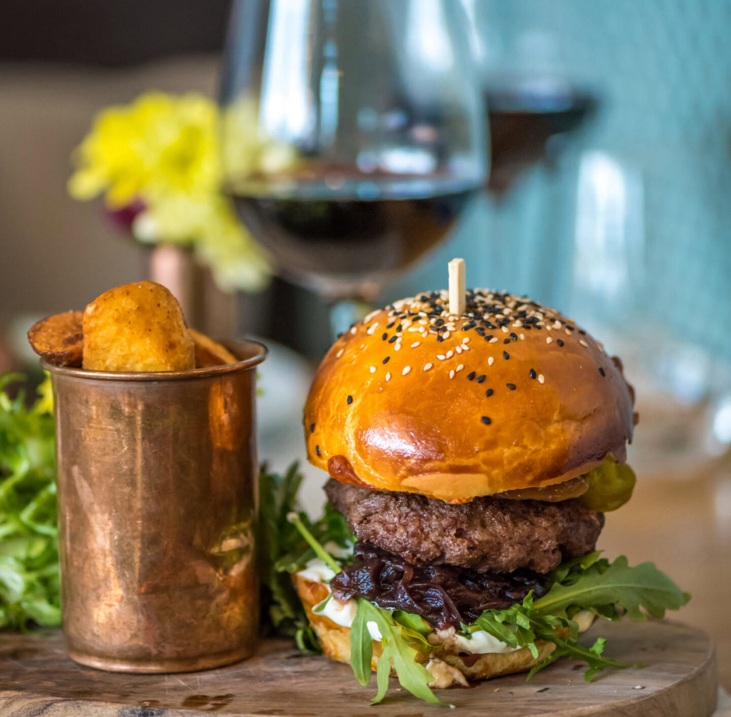 Gourmet burger with beef patty, lettuce, and bun, paired with a glass of red wine, on a rustic wooden table.