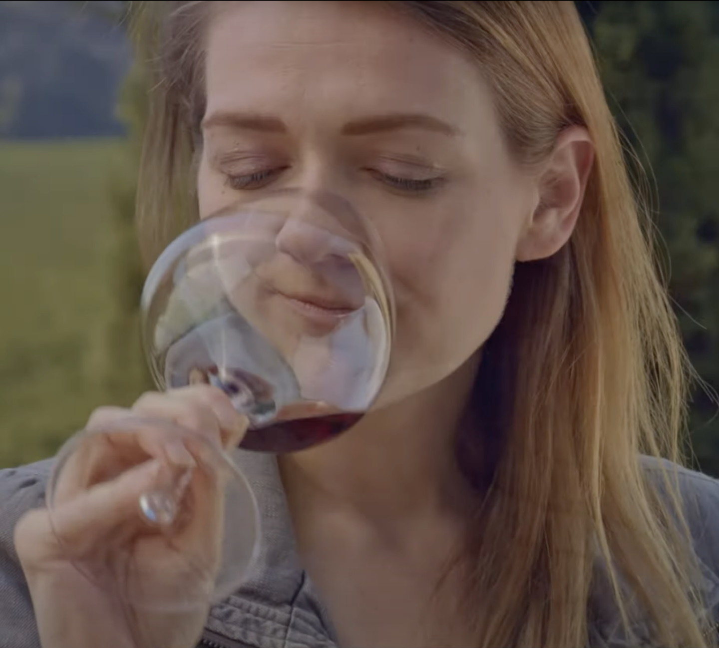 A woman enjoying wine tasting outdoors at Round Pond Estate, savoring a glass of red wine in a scenic vineyard setting.