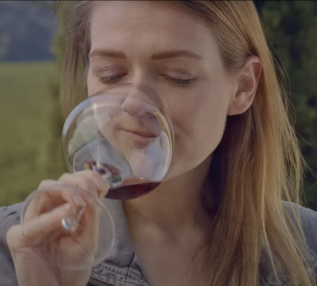 woman smelling her glass of wine with her nose partially in the glass