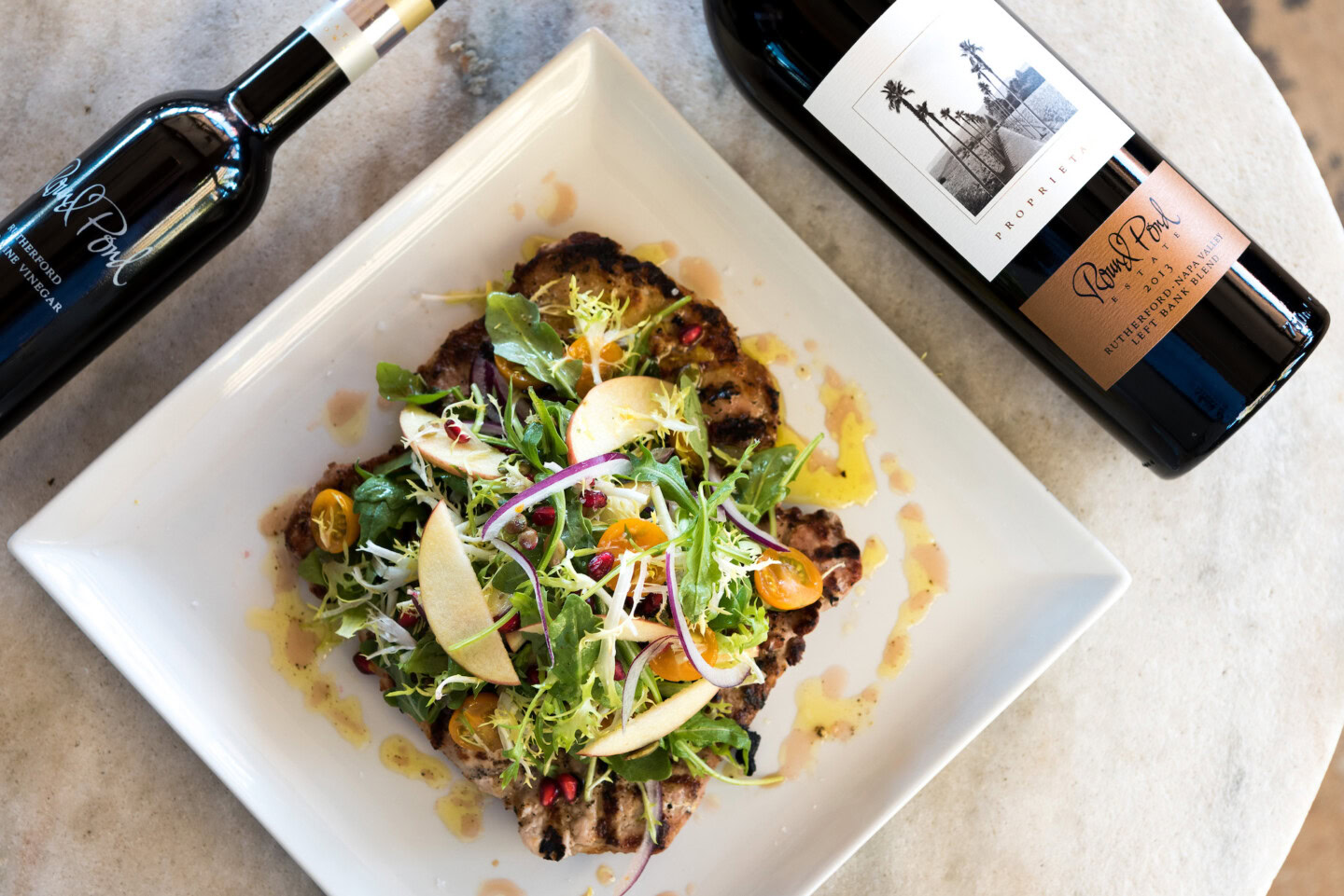Elegant salad with fresh greens, apple slices, and vinaigrette, paired with a bottle of red wine from Round Pond Estate.
