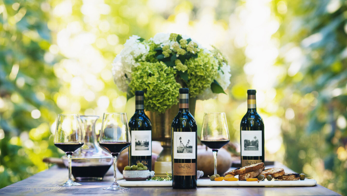 Elegant wine bottles and glasses set on a rustic table with a lush vineyard background.