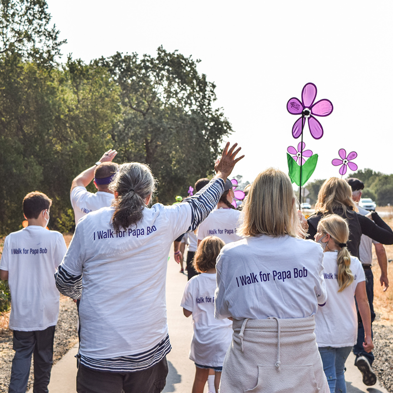 DSC_0945-(1) People walking to end Alzheimer's wearing white shirts with "I walk for Papa Bob" on the back and holding purple pinwheel flowers