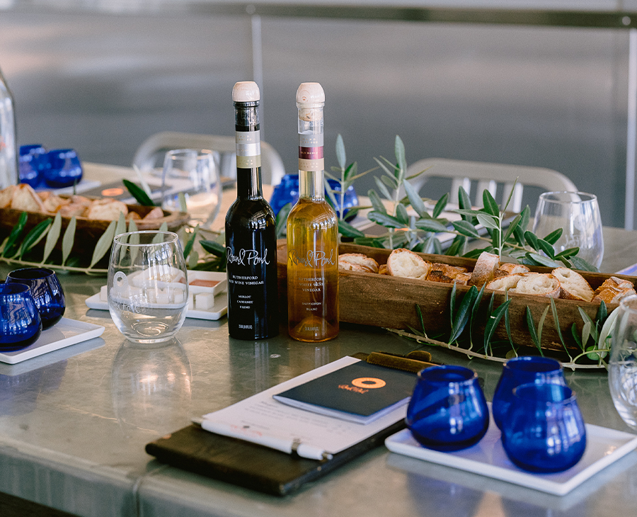 Olive oil tasting set up on chrome table with bottles, tasting menus, bread for dipping, and blue olive oil cups.