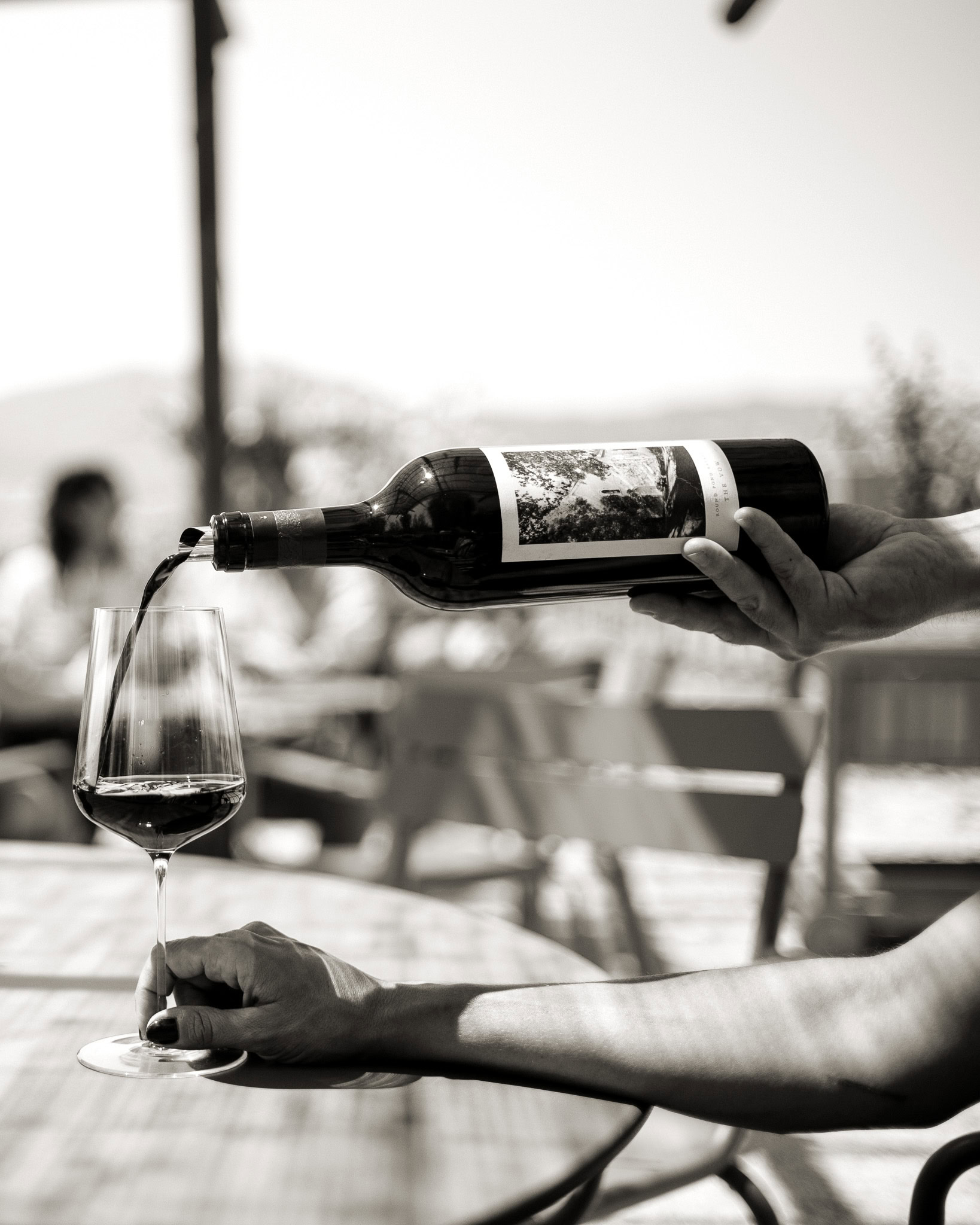 Hand pouring red wine into a glass outdoors at Round Pond Estate.