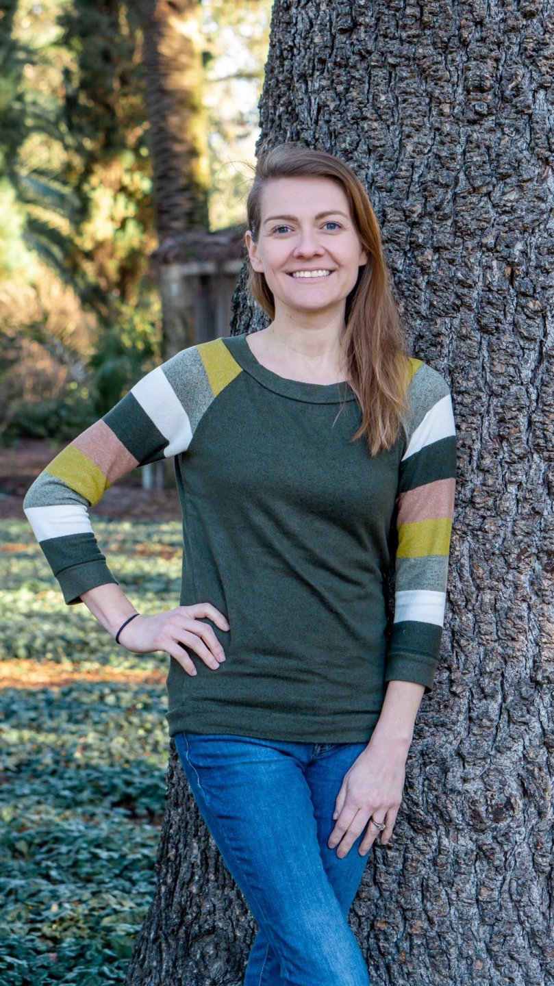 Young woman smiling outdoors near a tree, representing community and environmental awareness.