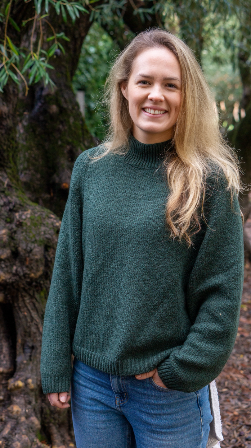 A woman smiling outdoors among trees, representing community and environmental awareness.