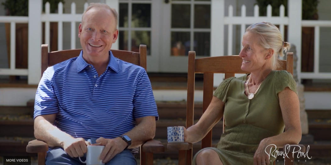 Ryan & Miles sitting in rocking chairs in front of a white deck, holding coffee cups and laughing.