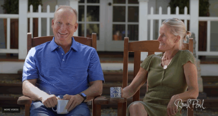 Screen Shot 2023-01-20 at 2.48.40 PM Ryan & Miles sitting in rocking chairs in front of a white deck, holding coffee cups and laughing.