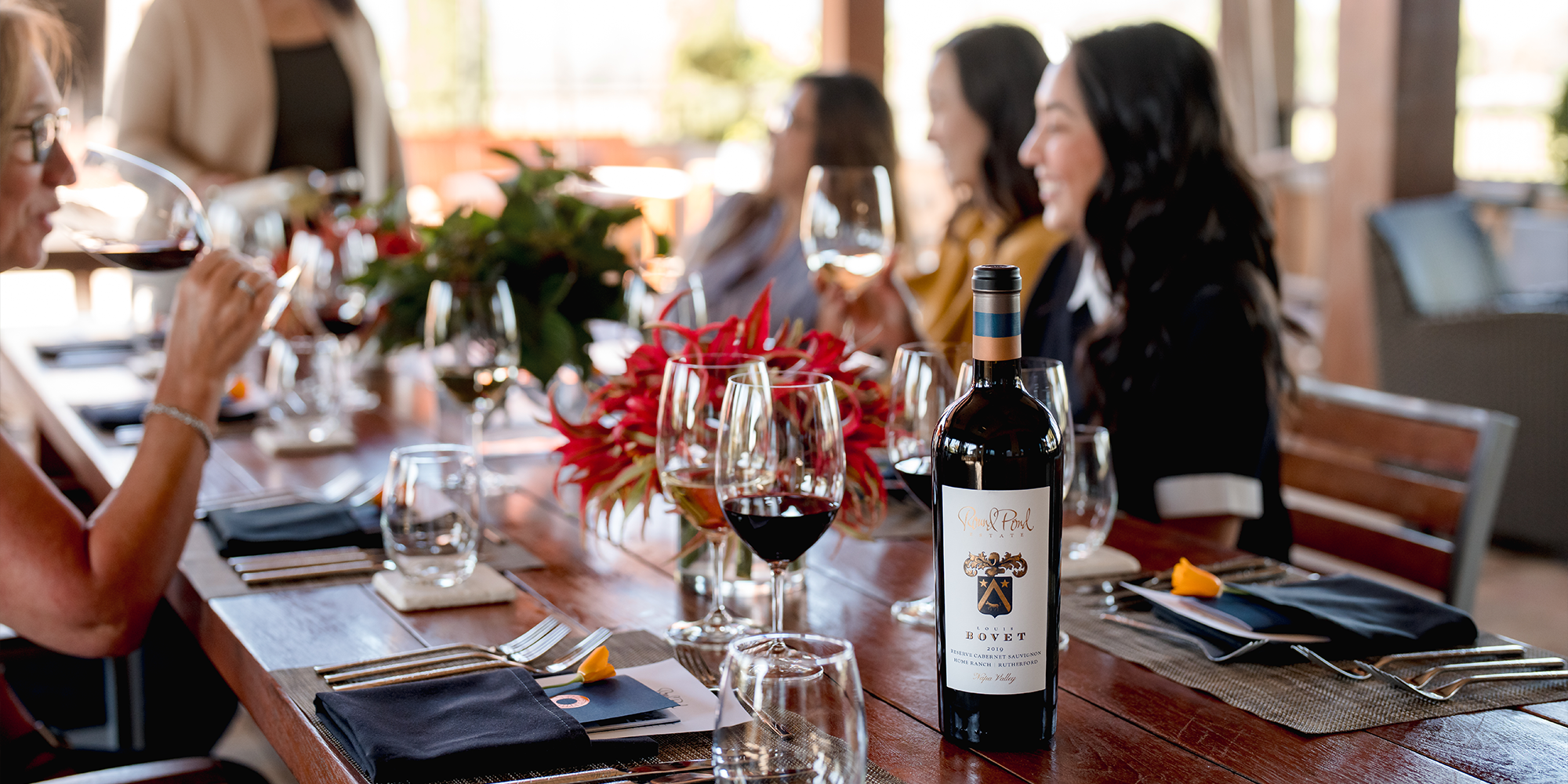 Guests gather a table with wine in hand. Louis Bovet Reserve Cabernet Sauvignon stands strong at the head of the table.