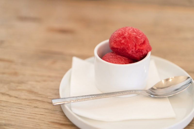 Delicious Rosato di Nebbiolo sorbet served in a white cup on a plate with a spoon, highlighting its vibrant pink color and re.