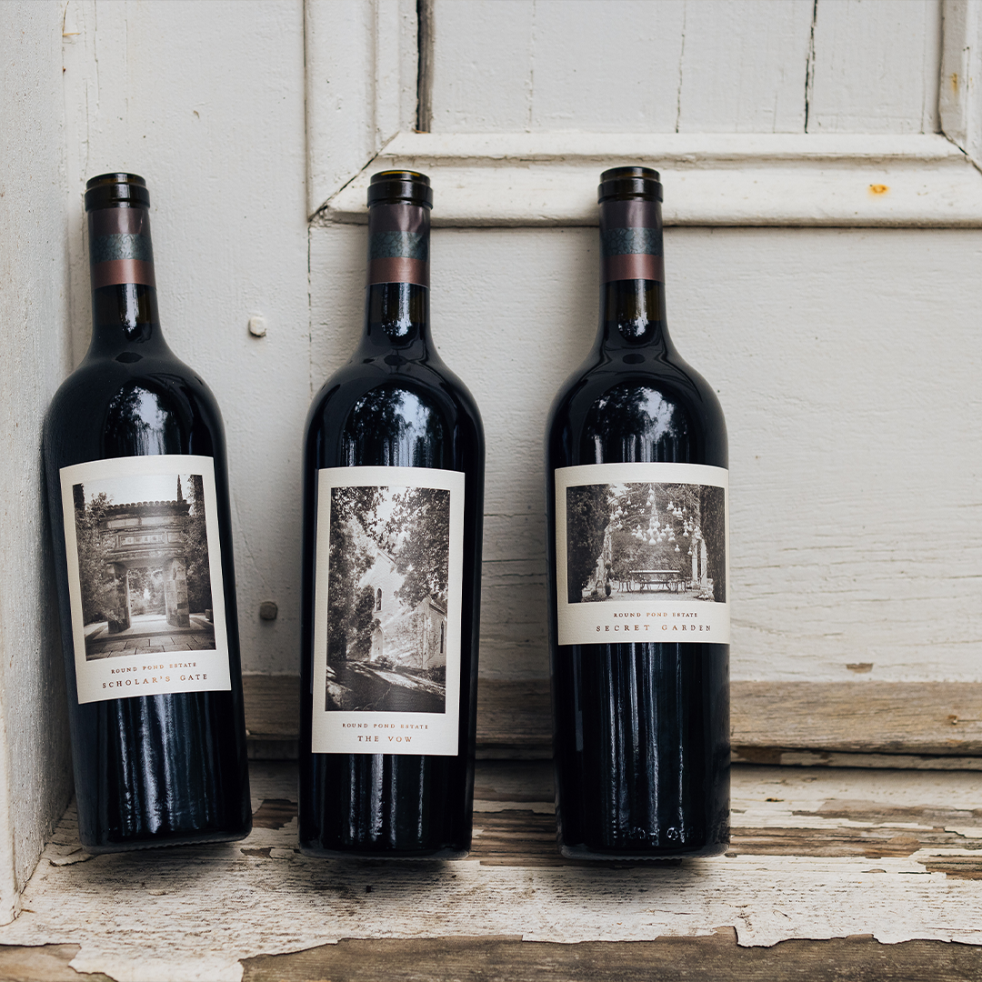 Three wine bottles with custom labels leaning against a rustic wooden surface.