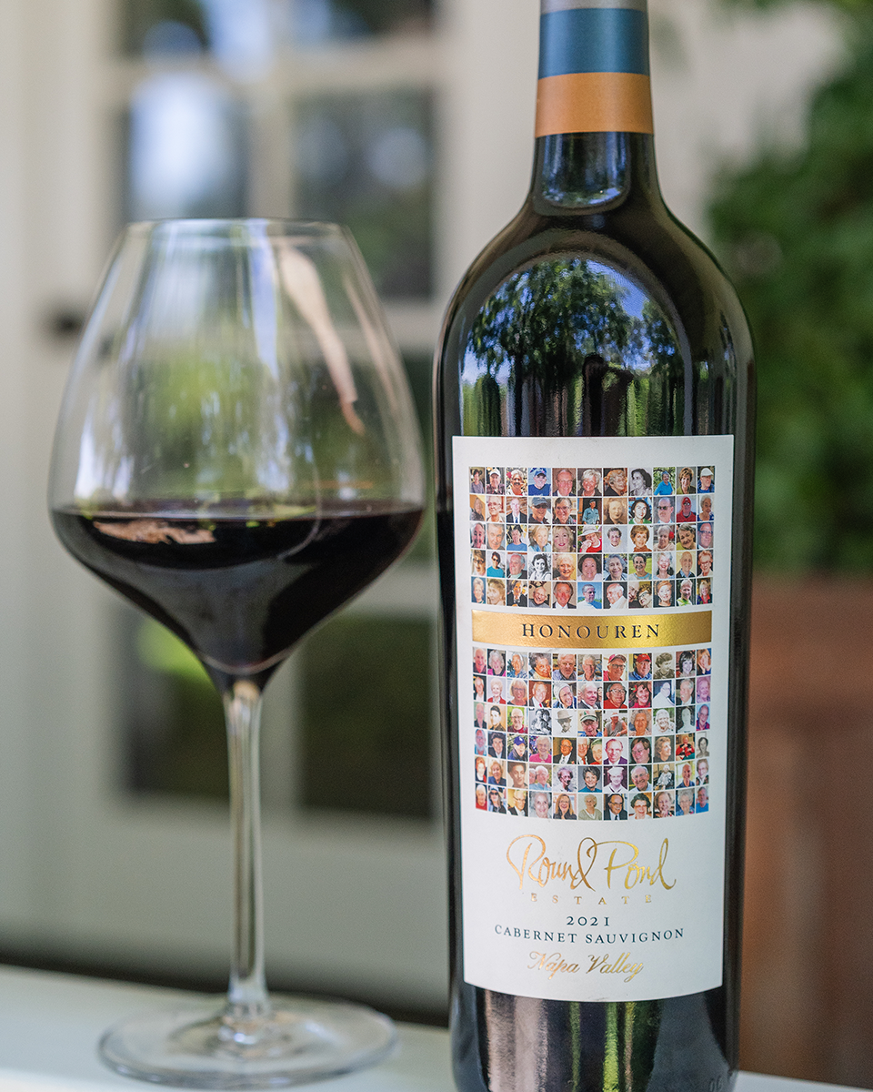 Glass of red wine next to a bottle of wine with a collage of images for the label.