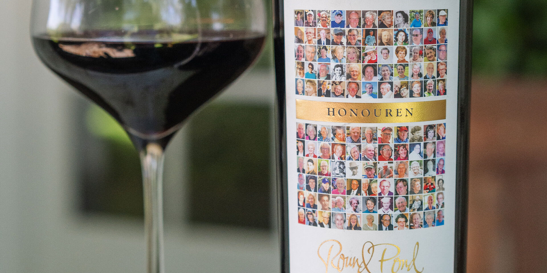 Glass of red wine next to a bottle of wine with a collage of images for the label.