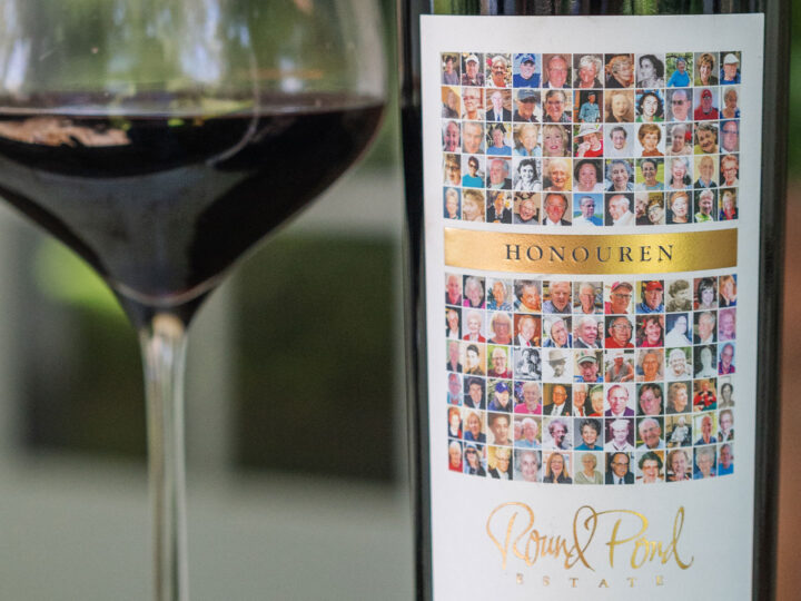 Glass of red wine next to a bottle of wine with a collage of images for the label.