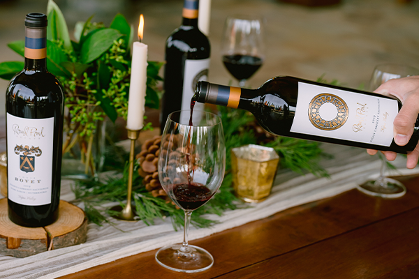 Red wine being poured into a class on a holiday table with greenery and candles