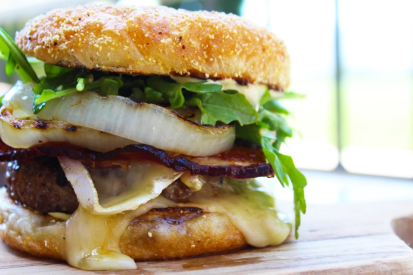 Delicious burger with melted cheese, crispy bacon, fresh greens, and grilled onion on a toasted bun. Perfect for BBQ enthusia.