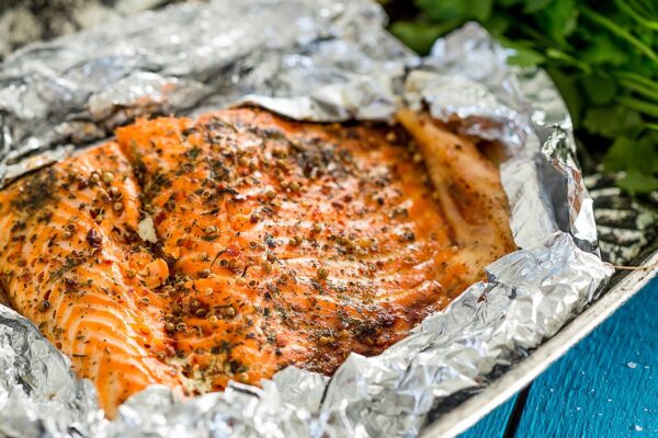 Succulent grilled salmon fillet seasoned with herbs, cooked in foil on a barbecue, ready for a delicious outdoor meal.