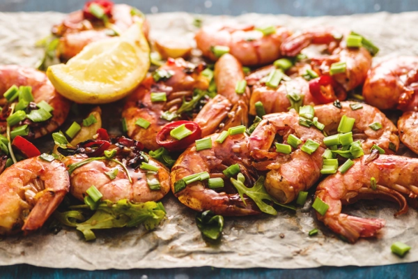 Grilled shrimp garnished with chopped green onions and lemon wedge, served on parchment paper.