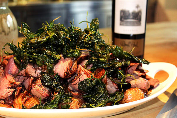 Succulent grilled meats topped with crispy, seasoned greens, served on a white platter at Round Pond Estate.