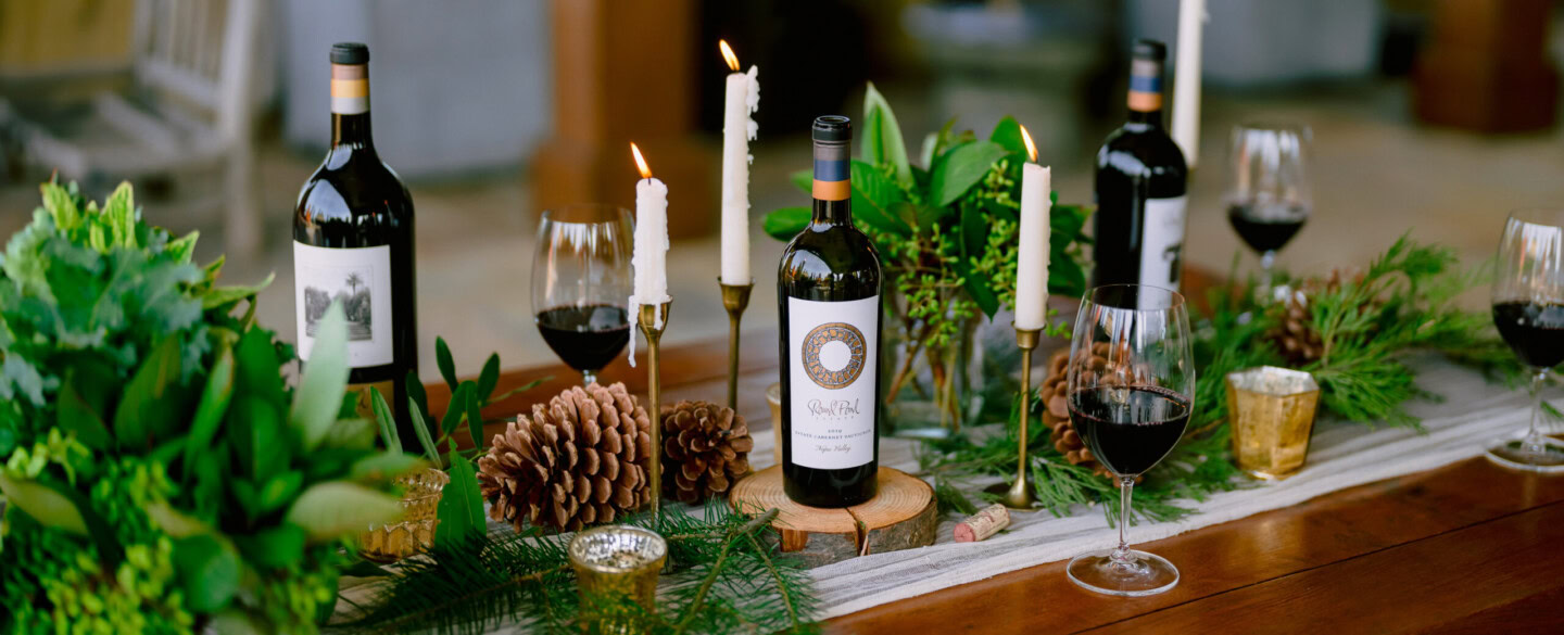 Elegant table setup at Round Pond Estate with wine bottles, candles, and festive greenery.