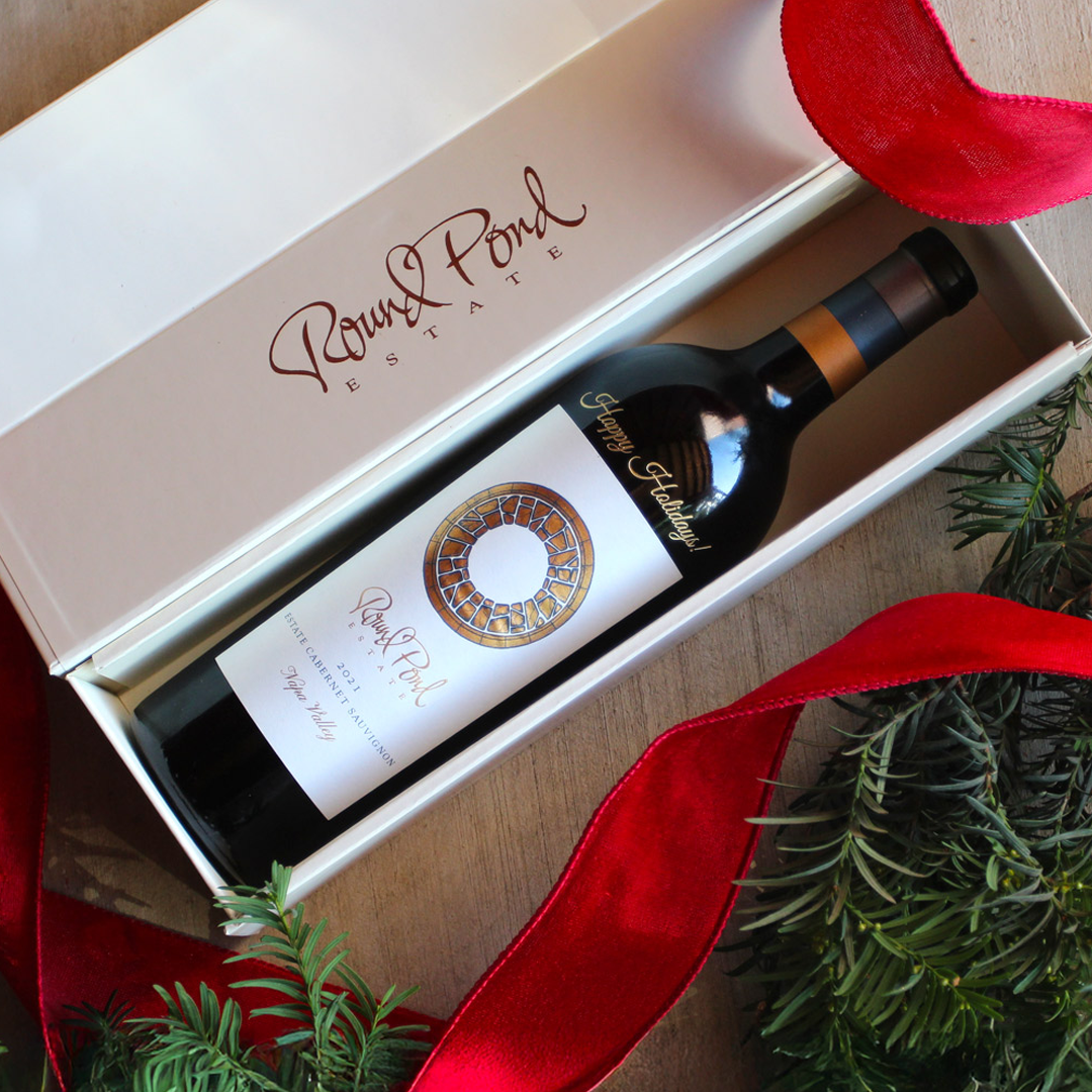 A bottle of Round Pond Estate wine presented in an elegant white box with the estate's logo, surrounded by festive red ribbon.