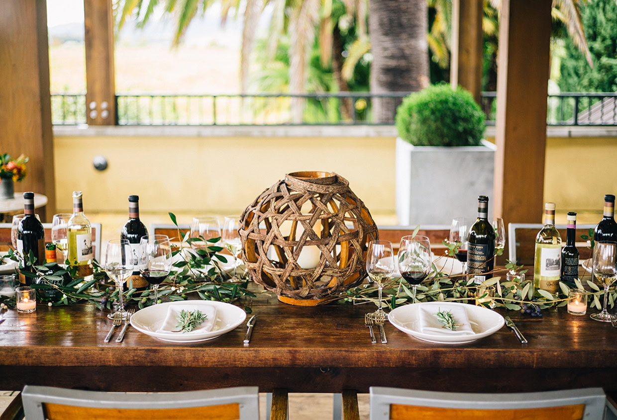 Elegant outdoor dining table with wine bottles, glassware, and greenery for a sophisticated wine-hosting experience.