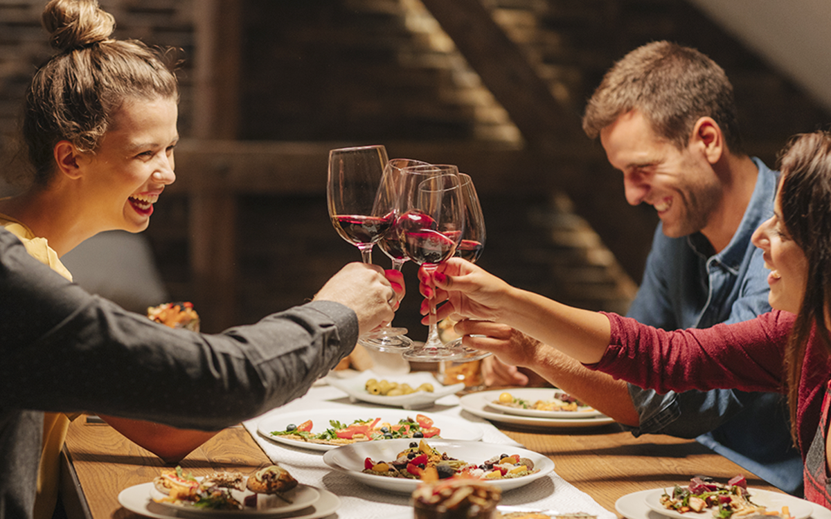 Group of friends clinking wine glasses during a celebration at Round Pond Estate, with food on the table, under warm lighting.