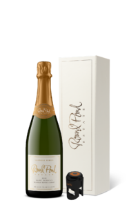 Bottle of sparkling wine next to a black champagne stopper in front of a cream gift box