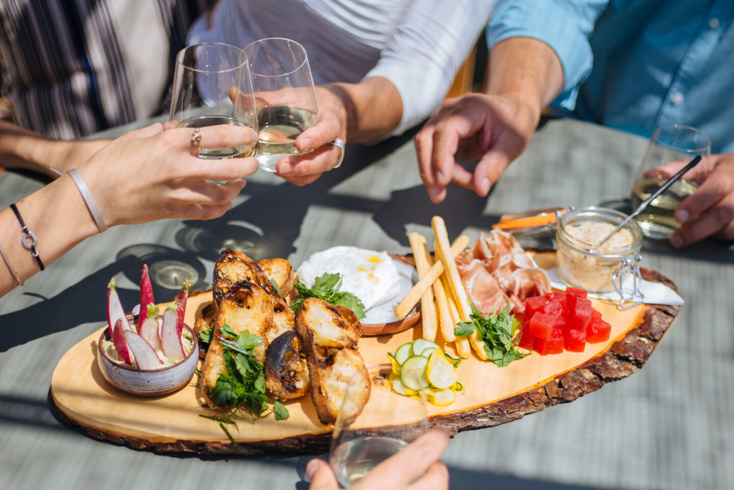 Enjoying wine with friends over a charcuterie board featuring cheese, fruits, and grilled chicken.