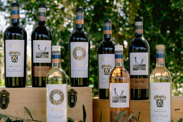 Collection of Round Pond Estate wines displayed outdoors with wooden boxes and greenery in the background.