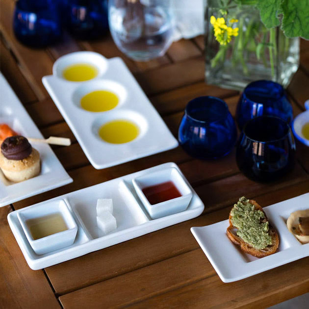 Olive oil tasting setup with small dishes of olive oils, bread, and condiments on a wooden table.