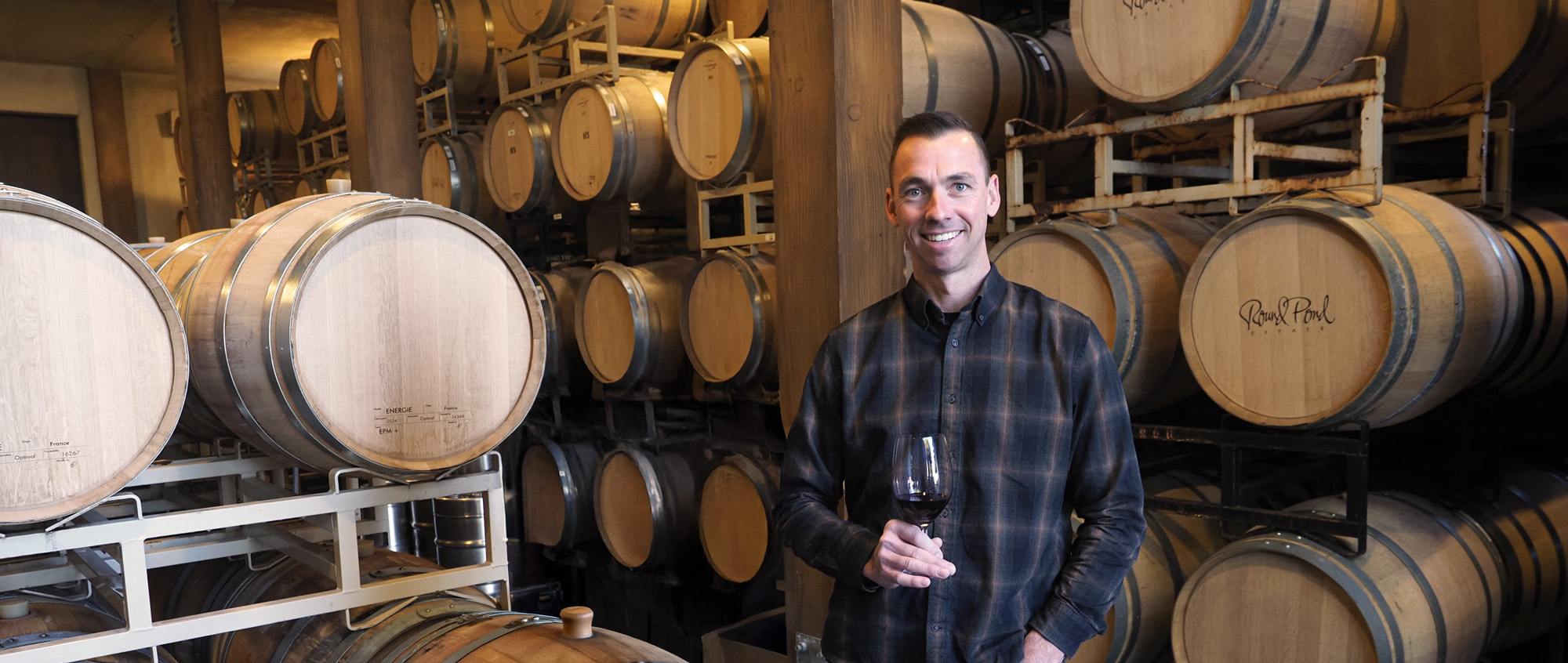 Jeff Plant Jeff Plant, Round Pond Estate Winemaker, stands in front of wine barrels with a glass of wine in hand.