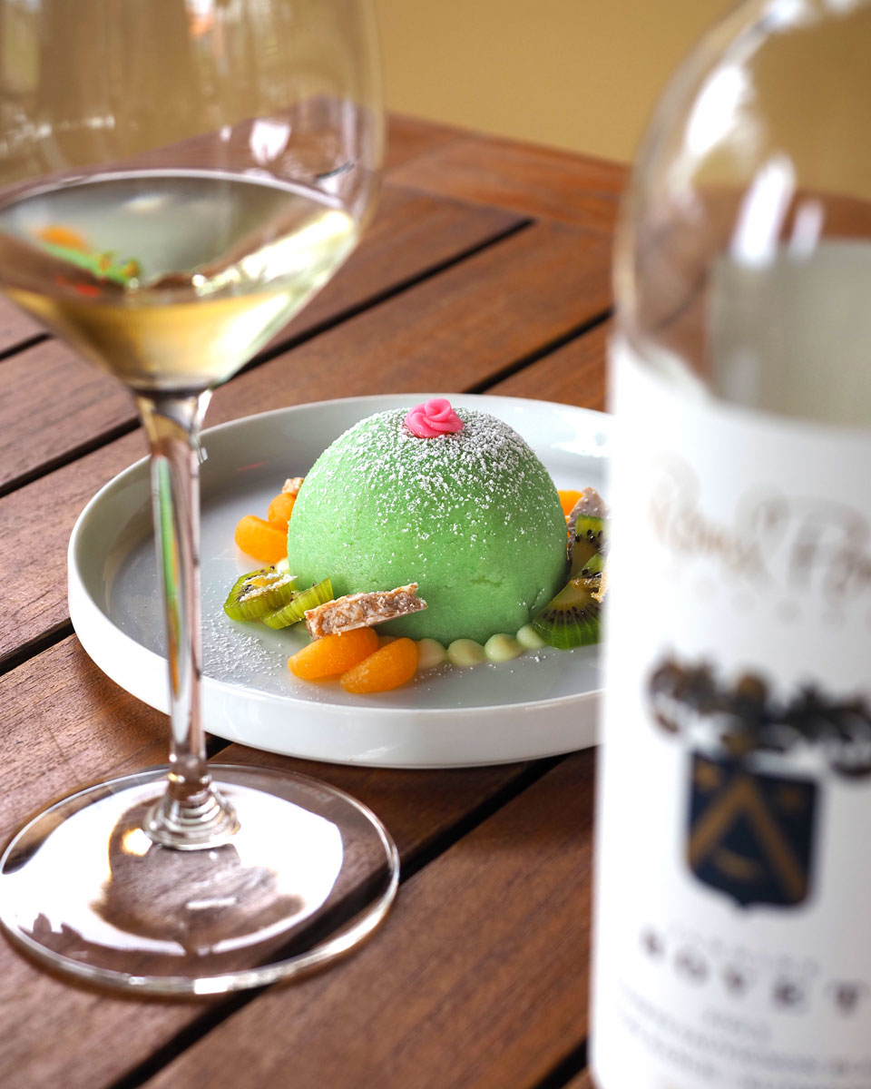 Round Pond Estate dessert pairing with white wine: pistachio mousse dome topped with powdered sugar, garnished with kiwi, mandarin orange, and almond brittle.