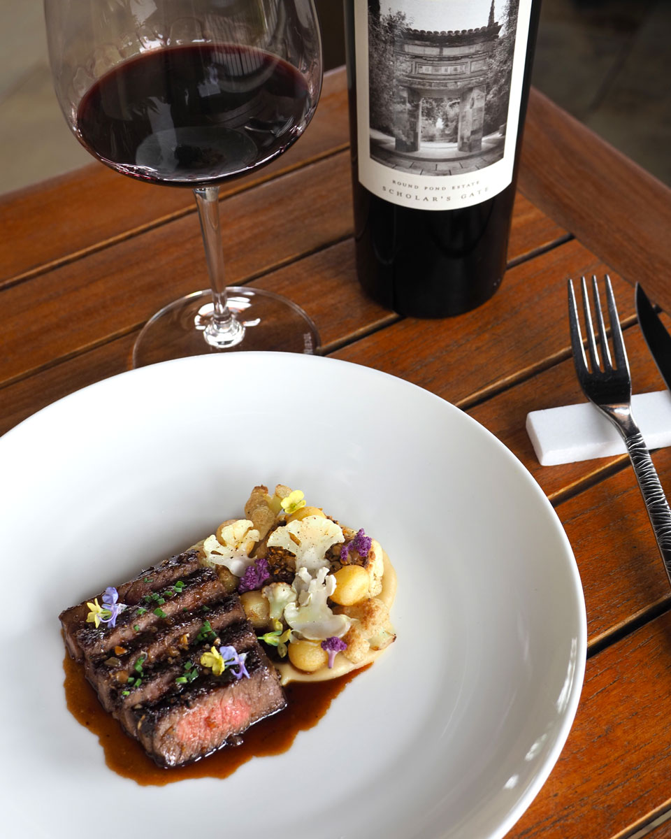 Wine-paired ribeye steak with roasted cauliflower and edible flowers, served with Round Pond Estate Scholars Gate Cabernet Sauvignon in Napa Valley.