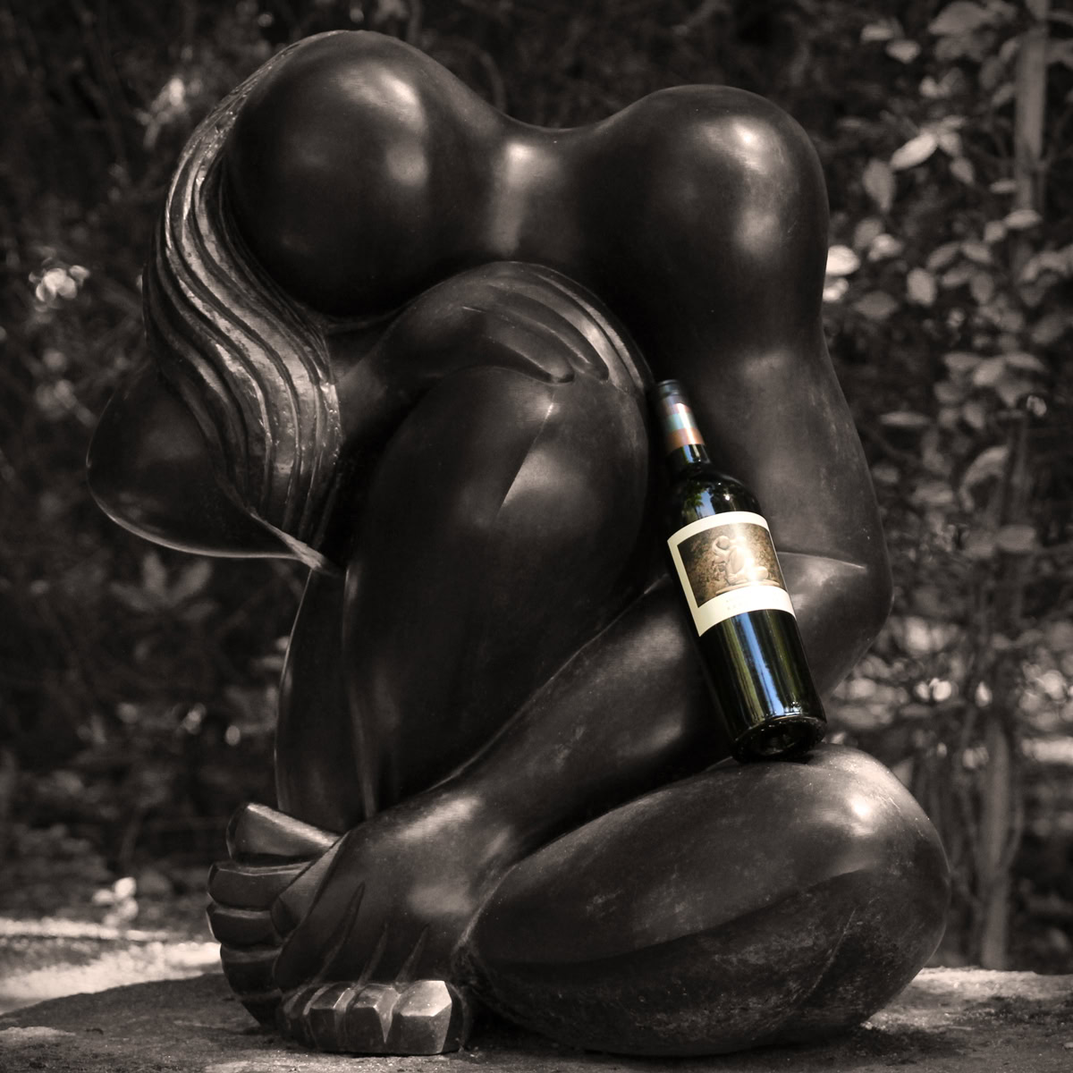 Artistic black sculpture of a woman holding a wine bottle, set outdoors at Round Pond Estate.