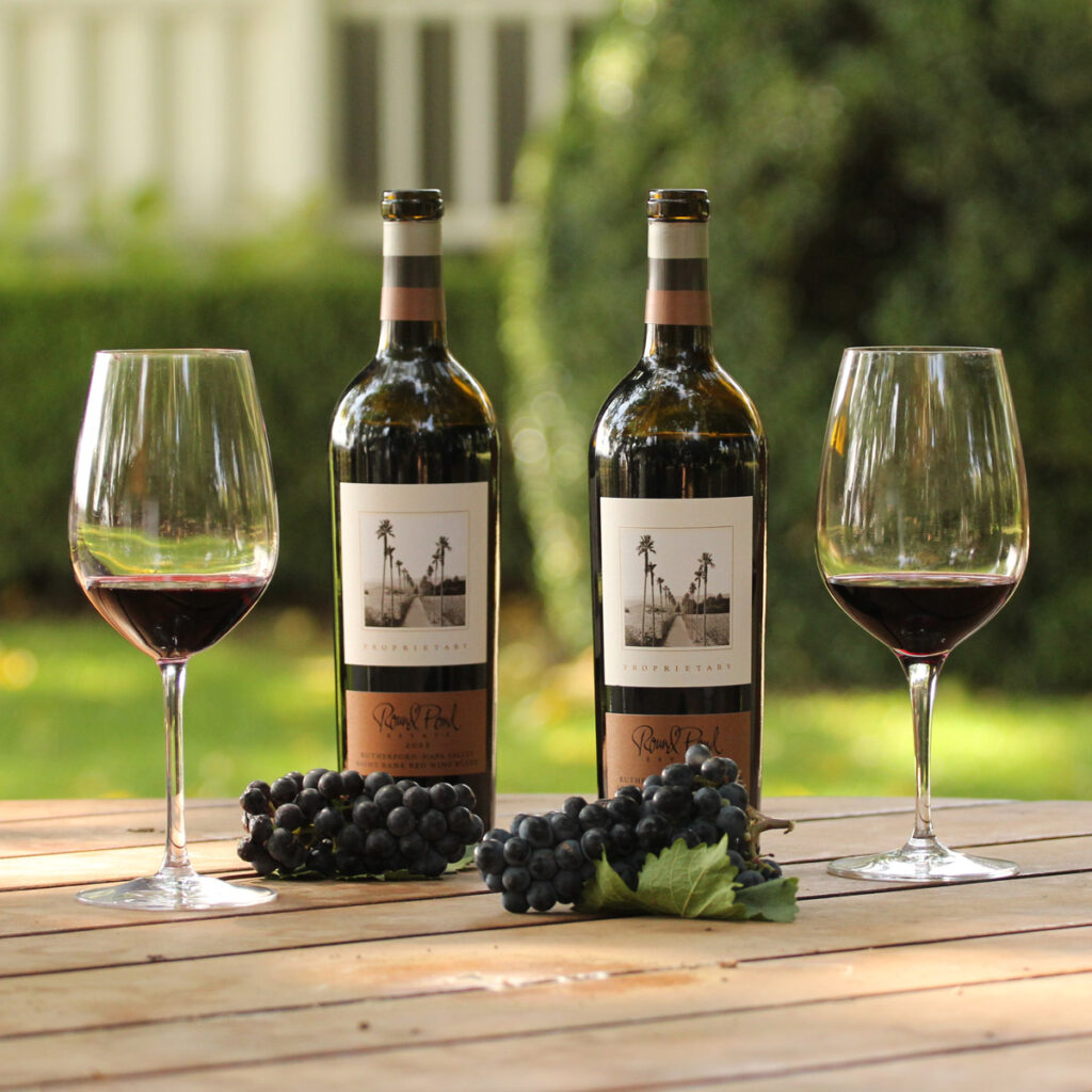 Two glass of red wine on a table next to bottles of Round Pond Estate's Proprietary Left Bank Blend and Proprietary Right Bank Blend.