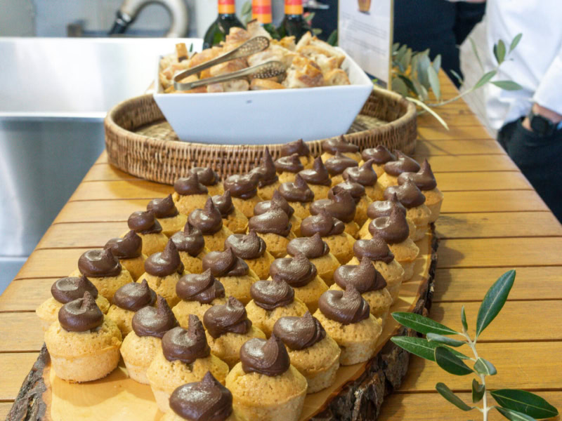 Hazelnut financier pastries topped with chocolate ganache displayed on a wooden table at Round Pond Estate.