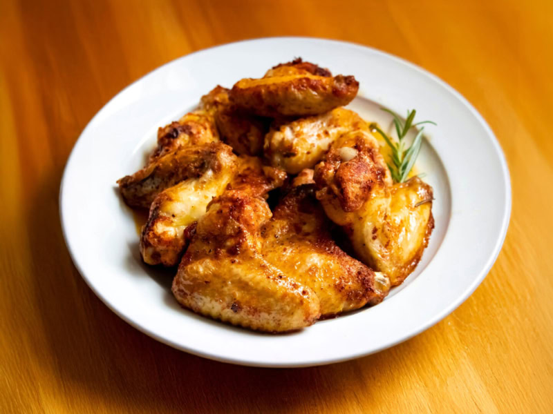 Delicious honey and smoked chili glazed chicken wings served on a white plate, garnished with fresh herbs.
