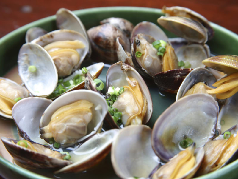 Clams served in a green bowl with white wine and saffron sauce, garnished with chopped green onions, showcasing a flavorful s.