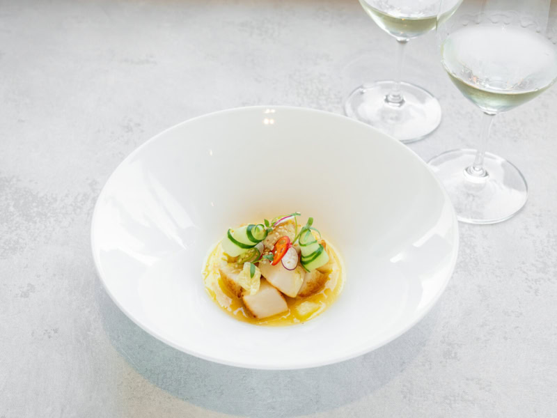 Roasted scallops served in a white bowl with citrus vinaigrette, garnished with sliced radishes and herbs, with two glasses o.