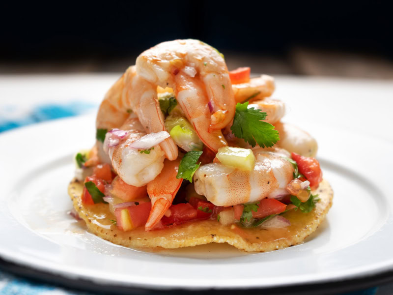 Delicious ceviche featuring fresh rock shrimp, blood orange segments, and chopped vegetables on a crispy tostada.