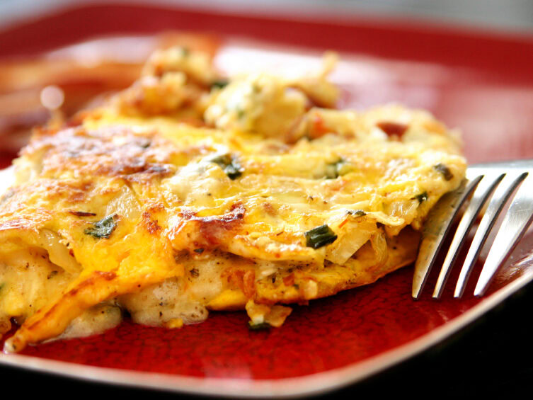 Scrambled eggs with chorizo, peppers, and cheese served on a red plate, garnished with herbs.