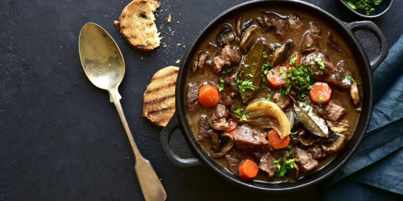 A hearty beef stew with vegetables in a rich wine sauce served in a cast iron skillet.