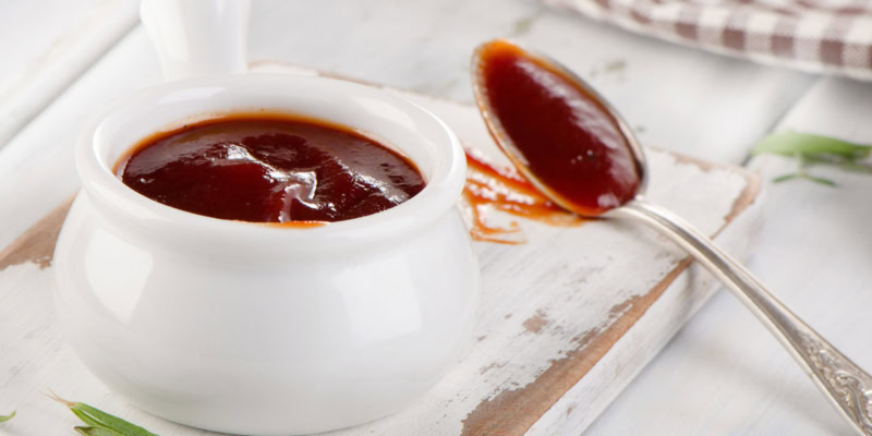 Rich Cab-Merlot BBQ sauce in a white bowl with a spoon on a rustic wooden surface.