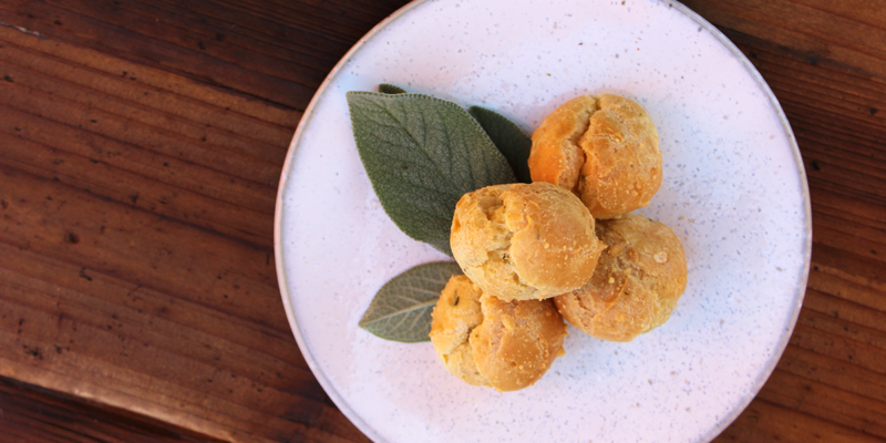 Delicious bacon and bleu cheese gougeres served on a white plate with fresh green leaves, perfect for appetizer or snack.