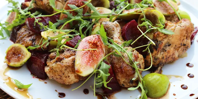 Delicious roasted chicken with figs, beets, and fresh greens on a white plate.